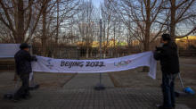 In der Nähe der Austragungsorte der Olympischen Winterspiele 2022 in Peking befestigen Arbeiter ein Transparent an einem Zaun. Foto: epa/Roman Pilipey