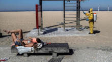eine Frau nimmt ein Sonnenbad, während ein Mann den Übungsplatz am Strand von Copacabana in Rio de Janeiro reinigt. Foto: epa/Antonio Lacerda