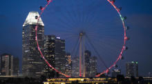 Das Singapur-Flyer-Riesenrad leuchtet am Abend vor der Skyline von Singapur. Foto: epa/How Hwee Young