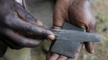 Ein traditioneller Beschneider schärft sein Messer, während die Jungen von ihren Vätern zum Gehöft in Bungoma geführt werden. Foto: epa/Stephen Morrison