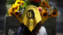 Ein junges Mädchen trägt einen Schal mit dem Schriftzug "Gerechtigkeit für Marielle" vor einem Blumengebinde. Foto: epa/Andre Coelho