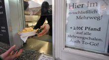 Eine Hand hält an einem Imbiss in der Innenstadt einen Mehrwegteller mit Pommes und einem Burger. Kunden haben künftig ein Anrecht darauf, ihre To-Go-Speisen und -Getränke in einer Mehrwegverpackung zu bekommen. Foto: Bernd Weißbrod/dpa