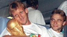 Andreas Brehme (l), damaliger deutscher Fußballnationalspieler, nimmt den WM-Pokal in den Arm und sein Teamgefährte Thomas Häßler schaut lächelnd zu. Foto: Frank Kleefeldt/dpa