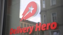 Logo und Schriftzug des Essenslieferdienstes Delivery Hero ist an einer Glasscheibe der Zentrale angebracht. Foto: Britta Pedersen/dpa-zentralbild/dpa