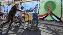 Menschen schieben ein Lastenfahrrad mit Wasserkanistern an einer mit Graffiti beschmierten Wand vorbei, während einer Solidaritätskampagne mit dem palästinensischen Volk. Foto: EPA-EFE/Yahya Arhab