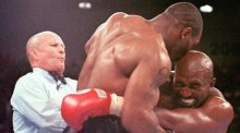 Der damalige Weltmeister im Schwergewicht, Evander Holyfield (r), verzieht das Gesicht, nachdem ihn sein Herausforderer Mike Tyson (M) ins Ohr gebissen hat. Foto: Jeff Haynes/epa
