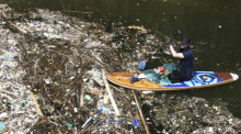 Ein Freiwilliger, der auf einem Paddelbrett sitzt, sammelt auf einem Fluss in Pecatu Müll auf. Während der Monsunzeit sind einige Flüsse mit Plastikmüll und Unrat übersät. Foto: Firdia Lisnawati/Ap/dpa