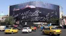 Fahrzeuge passieren auf dem Enghelab-Platz in Teheran ein antiamerikanisches Plakat mit einer Darstellung von US-Präsident Donald Trump. Foto: Abedin Taherkenareh/epa