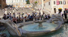 Touristen sitzen im Schatten an der Fontana della Barcaccia, ein Brunnen auf der Piazza di Spagna, vor der Spanischen Treppe. Foto: Robert Messer/dpa