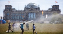 Menschen kühlen sich an Wassersprinklern vor dem Reichstagsgebäude in Berlin während der Hitzewelle ab. Foto: EPA/Clemens Bilan