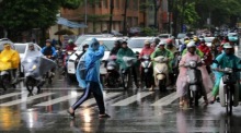 Menschen auf Motorrädern warten im Regen an einer Ampel in Hanoi nach dem Durchzug des Taifuns Bualoi. Foto: epa/Luong Thai Linh