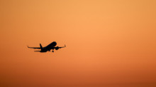 Ein Flugzeug hebt vor orangefarbenem Himmel ab. Foto: Jan Woitas/dpa/dpa-tmn