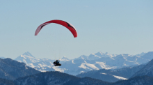 Ein Paraglider fliegt vom Brauneck-Gipfel aus und ist vor der Kulisse von Hoher Tenn und Großes Wiesbachhorn zu sehen. Foto: Tobias Hase/dpa