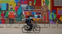 In Indien fahren Radfahrer mit Gesichtsschutzmasken an einem Wandgemälde in Bangalore vorbei. Foto: epa/Jagadeesh Nv