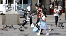 Ein Kind und eine Frau mit Gesichtsmasken spazieren zwischen Tauben in Zagreb. Foto: epa/Antonio Bat