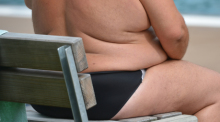 Ein übergewichtiger Mann sitzt in einem Freibad. Foto: Franziska Kraufmann/dpa