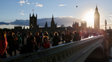 Zahlreiche Menschen stehen in der Abendsonne auf der im Augenblick für den Verkehr gesperrten Westminster Bridge über der Themse vor dem Parlament. Foto: Christian Charisius/dpa