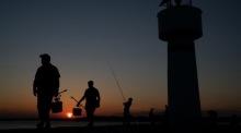 Fischer laufen bei Sonnenuntergang nahe des Bosporus in Istanbul entlang eines Leuchtturms während der Corona-Pandemie. Foto: epa/Sedat Suna