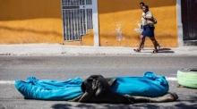 Zwei Leute gehen neben der Leiche eines Menschen auf einer Straße in Port-au-Prince. Foto: epa/Mentor David Lorens