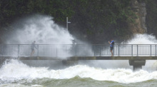 Menschen beobachten, wie Wellen gegen die Klippen eines Strandes schlagen. Foto: Brett Phibbs/Nz Herald/ap/dpa