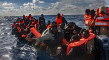 Mehrere Migranten sitzen in einem Boot im Mittelmeer, während Rettungskräfte versuchen ihnen zu helfen. Foto: Antonio Sempere/Europa Press/dpa