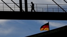 Ein Passant geht über eine Brücke im Berliner Regierungsviertel, während im Hintergrund die deutsche Flagge flattert. Foto: epa/Filip Singer