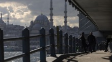 Menschen überqueren die Galata-Brücke in Istanbul am Goldenen Horn unter grauem Himmel und zeigen den Alltag der Stadt heute dort. Foto: epa/Tolga Bozoglu