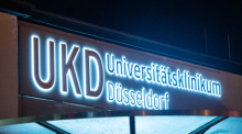 Das Logo des Universitätsklinikums Düsseldorf UKD leuchtet an einem Eingang des Krankenhauses. Foto: Christophe Gateau/dpa