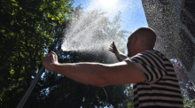 Ein Mann erfrischt sich in einem Garten mit Wasser aus einem Gartenschlauch. Foto: Karl-Josef Hildenbrand/dpa