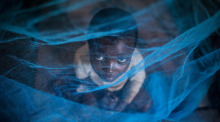 Ein Flüchtlingskind aus Burundi sitzt in Gashora, Ruanda, unter einem Moskitonetz. Foto: Dai Kurokawa/epa/dpa