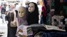 Eine Frau mit einer Schutzmaske geht in einem Textilgeschäft in der Innenstadt von Amman an Schaufensterpuppen mit Kopftüchern vorbei. Foto: epa/Andre Pain