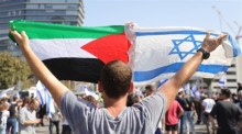 Ein Mann hält die israelische und die palästinensische Flagge hoch, als Demonstranten während einer Anti-Regierungs-Demonstration in Tel Aviv die Ayalon Road im Zentrum blockieren. Foto: epa/Abir Sultan