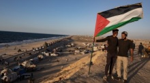 Zwei Männer mit palästinensischer Flagge begleiten Vertriebene, die entlang der Küstenstraße Al-Rashid in Richtung Gaza-Stadt ziehen. Foto: epa/Haitham Imad