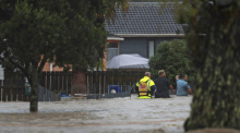 Rettungskräfte und ein Mann waten durch das Hochwasser einer überschwemmter Straße. Foto: Hayden Woodward/New Zealand Herald/ap/dpa