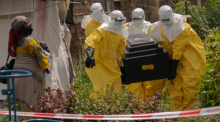 Eine Frau weint, als Mitarbeiter des Roten Kreuzes in Schutzanzügen den Sarg einer an Ebola verstorbenen Person aus einem Gesundheitszentrum in Rwampara tragen. Foto: Moses Sawasawa/Ap/dpa