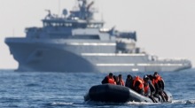 Die Migranten überqueren den Ärmelkanal in einem kleinen Boot, mit einem französischen Kriegsschiff im Hintergrund. Foto: epa/Tolga Akmen