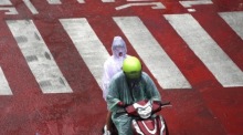 Ein Motorrollerfahrer und sein Sozius fahren bei Regen über eine Straße in Bangkok. Für Donnerstag werden in der Hauptstadt vor allem am Nachmittag und Abend weitere Schauer und Gewitter erwartet. Foto: epa/Rungroj Yongrit