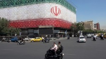 Autofahrer passieren den Enqelab-Platz in Teheran mit einer großen Darstellung der iranischen Nationalflagge im Hintergrund. Foto: epa/Abedin Taherkenareh