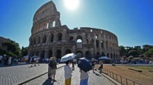 Besucher schützen sich mit Schirmen vor der Sommerhitze am Kolosseum in Rom. Foto: Ettore Ferrari/epa