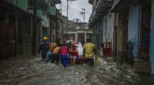 Männer schieben eine Frau in ihrem Boot durch eine von heftigen Regenfällen überflutete Straße. Foto: Ramon Espinosa/dpa