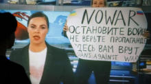 TV-Sendung, in der ein Angestellter das Ostankino-Fernsehstudio mit einem Plakat betritt, auf dem steht: 