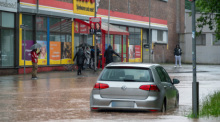 Passanten stapfen und fahren durch das Hochwasser in der Fischbachstrasse in Saarbrücken. Nach starken Regenfällen steht diese teilweise unter Wasser. Foto: Harald Tittel/dpa