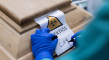 Ein Bestattungsunternehmer schreibt «C19» auf ein Schild mit dem Hinweis «Infektiös» auf einen Sarg mit einem Verstorbenen, der an dem Coronavirus gestorben ist. Foto: Rolf Vennenbernd/dpa