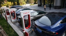 Menschen gehen an Elektroautos von Tesla vorbei, die an einer Ladestation in Peking aufgeladen werden. Foto: EPA-EFE/Roman Pilipey