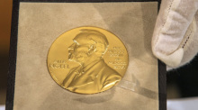 Eine Hand hält vor der Übergabe des Nobelpreises für Physik an den deutschen Physiker Genzel die goldene Medaille. Foto: Peter Kneffel/dpa/pool/dpa