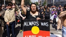 Ein Demonstrant trägt ein Plakat mit der Flagge der Aborigines während einer Kundgebung zum Invasionstag in Sydney. Foto: epa/Diego Fedele