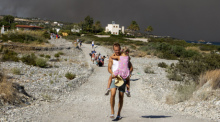 Ein Mann trägt ein Kind, als sie ein Waldbrandgebiet verlassen. Foto: Lefteris Damianidis/Intime News/ap/dpa
