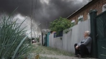Ein Einwohner sitzt in der Nähe seines Hauses, während nach russischem Beschuss in Charkiw Rauchwolken über der Stadt aufsteigen. Foto: epa/George Ivanchenko