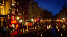 Menschen schlendern am Abend an einer Gracht entlang durch den Rotlichtbezirk De Wallen. Foto: Koen Van Weel/epa/dpa