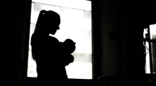 Eine Frau steht mit einem Neugeborenen am Fenster einer Klinik. Foto: Sina Schuldt/dpa